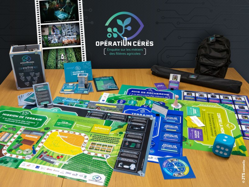 Photo d'une table avec les &eacute;l&eacute;ments du jeu p&eacute;dagogique &agrave; disposition. Des plateaux de jeu, des cartes, des pions et des d&eacute;s sont en &eacute;vidence avec le logo du jeu en haut de l'image (Op&eacute;ration C&eacute;r&egrave;s - enqu&ecirc;te sur les m&eacute;tiers des fili&egrave;res agricoles).